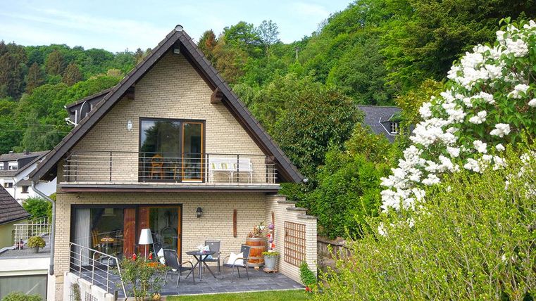 Ein wunderschönes, modernes Haus umgeben von grüner Natur. Auf der Terrasse stehen Möbel und Pflanzen, die eine einladende Atmosphäre schaffen.