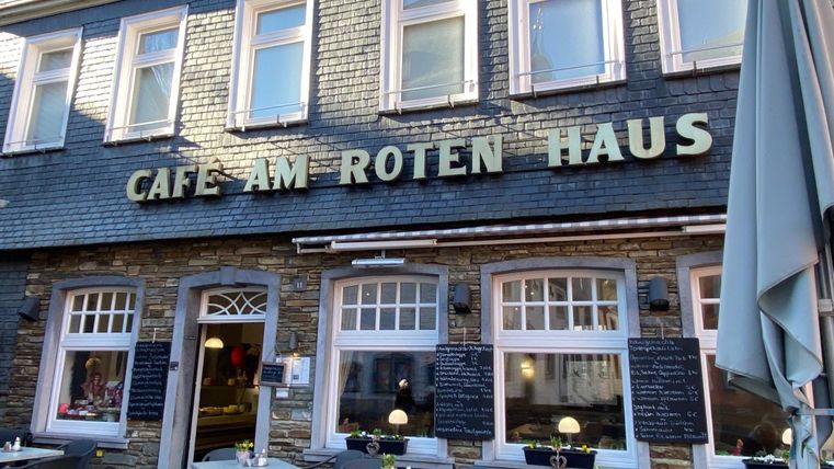A cozy café named "Café am Roten Haus". There are tables outside and an inviting atmosphere.