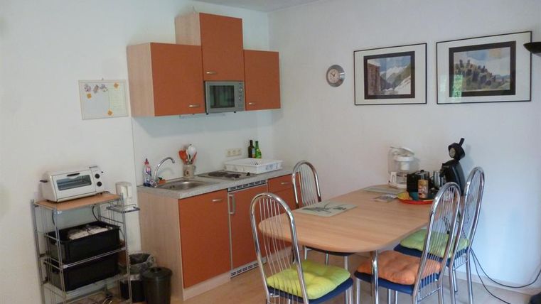 Een moderne keuken met houten kasten en lichte muren. Het eetgedeelte heeft een ovale tafel met kleurrijke stoelen en verschillende keukenapparaten.