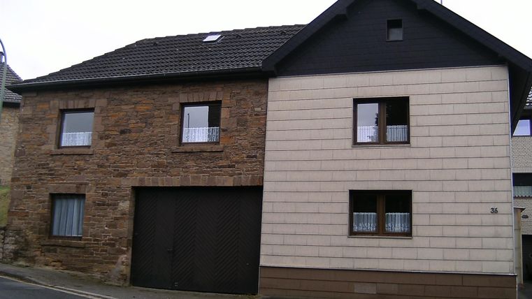 Ein zweigeschossiges Haus mit einer Kombination aus Stein- und Putzfassade. Die Struktur hat ein Satteldach und mehrere Fenster.