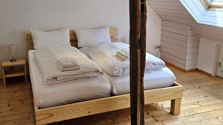 A cozy bedroom with a double bed and wooden floor. The room has large windows with plenty of daylight.