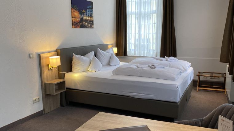 A modern hotel room with two beds, nightstands, and a desk. Bright curtains and a picture on the wall create a friendly atmosphere.