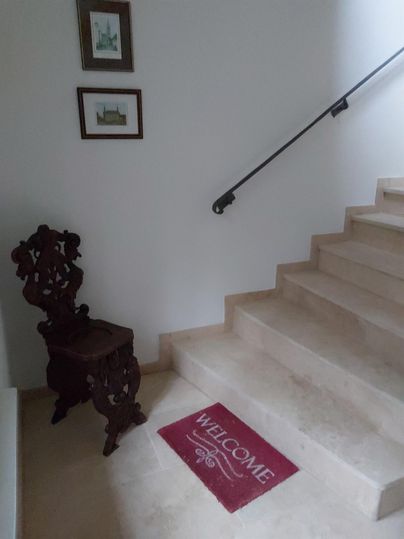 Een uitnodigende entree met een trap en een houten stoel. Op de vloer ligt een welkomstmat.