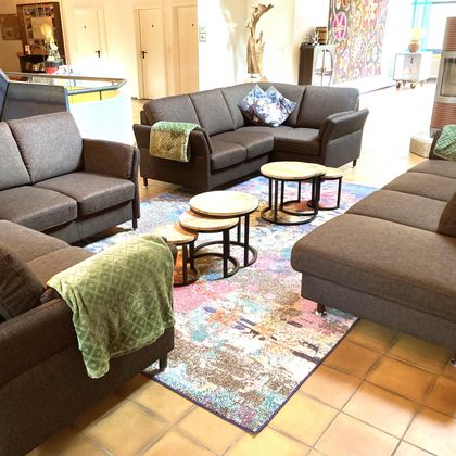 A cozy seating area with several gray sofas and coffee tables. The floor is decorated with a colorful rug, and a green throw is on one of the sofas.