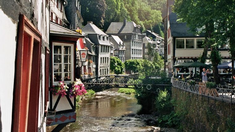 A picturesque town with traditional houses by the river. Trees surround the scene, creating a tranquil atmosphere.