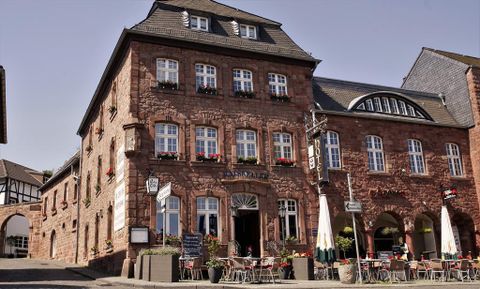 Een traditioneel gebouw met een rode stenen gevel en vele ramen. Voor het huis staan tafels en stoelen die uitnodigen om te verblijven.