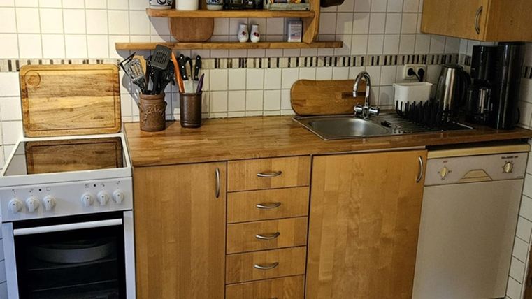 A modern kitchen with wooden surfaces and white tiles. There is a stove, a sink, and a dishwasher.
