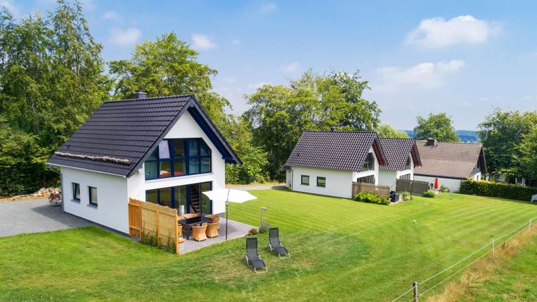 Various modern houses stand in a green landscape. The sky is clear and sunny, perfect for relaxing days outdoors.