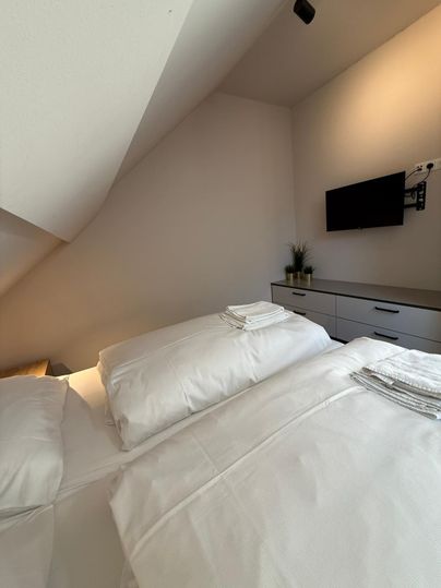 Een gezellige kamer met twee bedden en frisse beddengoed. Aan de muur hangt een televisie, en er is een eenvoudige commode met planten.