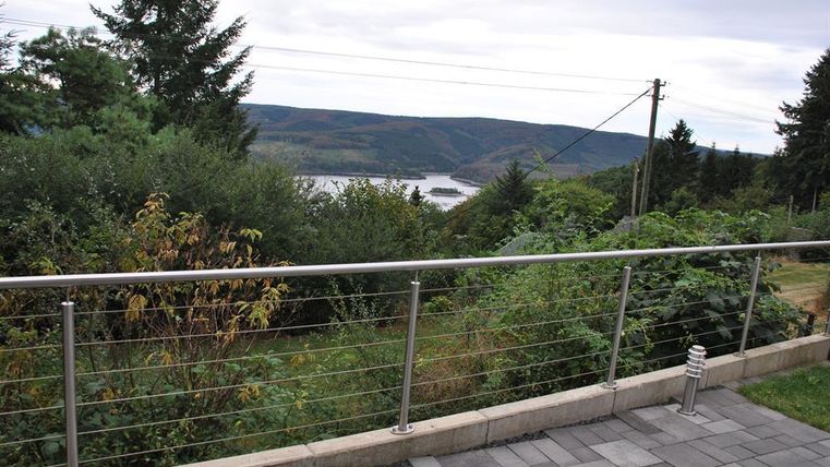 Een prachtig uitzicht over groene heuvels en een rivier. Op de voorgrond bevindt zich een modern hek en een bestrating.