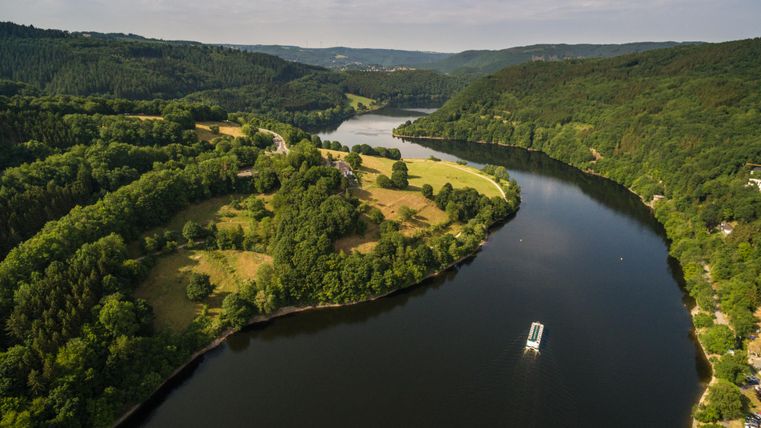 A picturesque river landscape with gentle hills and lush greenery. A boat glides peacefully on the water.