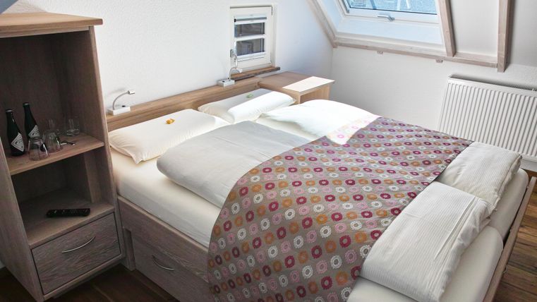 A cozy bedroom with a double bed and colorful bedspreads. Next to the bed is a wooden wardrobe with some accessories.