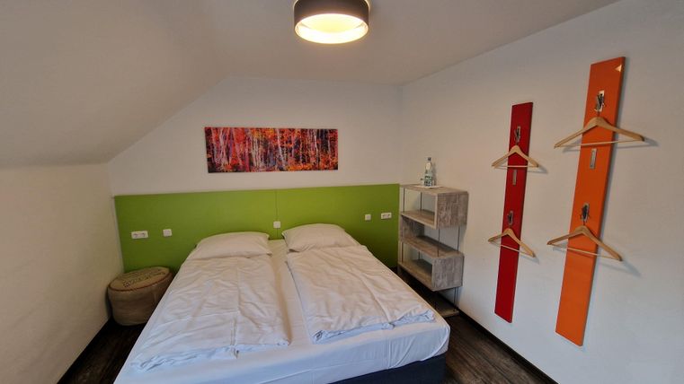 A modern bedroom with a double bed and colorful walls. There are practical storage surfaces and decorative elements.