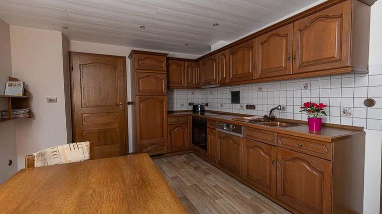 Eine moderne Küche mit Holzschränken und hellen Fliesen. Ein Tisch aus Holz steht in der Mitte des Raumes.