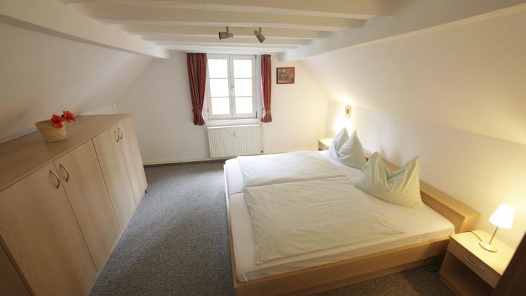 Een gezellige slaapkamer met een tweepersoonsbed en houten kasten. Heldere muren en zacht licht creëren een ontspannen sfeer.