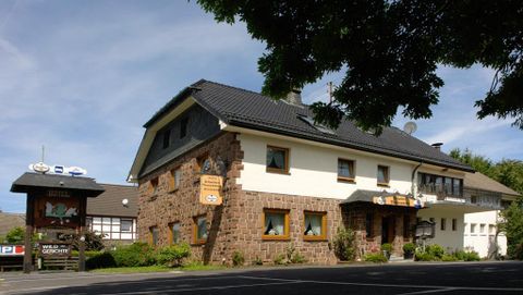 A traditional inn with a rustic facade of stone and wood.
Surrounded by green vegetation and a clear blue sky.