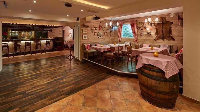 Ein gemütliches Restaurant mit Holzmöbeln und rustikaler Dekoration. Der Raum ist mit Tischen und Stühlen eingedeckt und hat eine einladende Atmosphäre.