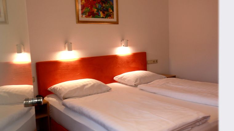 A cozy bedroom with two single beds and modern wall lamps. A colorful painting hangs on the wall, making the room feel lively.