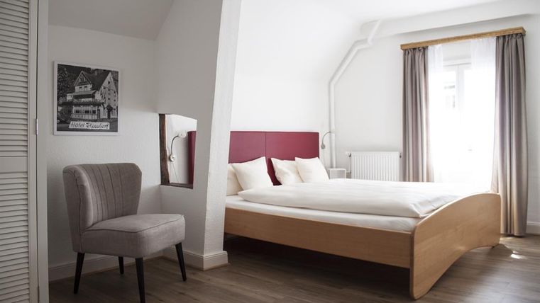 Een moderne slaapkamer met een comfortabel bed en een lichte kleurstelling. Een comfortabele stoel en een raam met gordijnen maken de ruimte compleet.