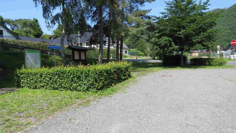 Een rustige straat met een grindoppervlak, omgeven door bomen en struiken. Op de achtergrond zijn enkele gebouwen en een speeltuin te zien.