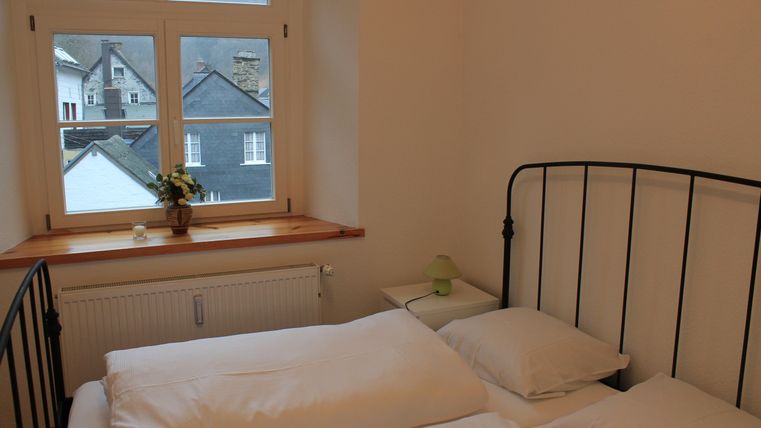 Een gezellige slaapkamer met een zwart bed en witte beddengoed. Vanuit het raam is een uitzicht op andere huizen en het landschap zichtbaar.