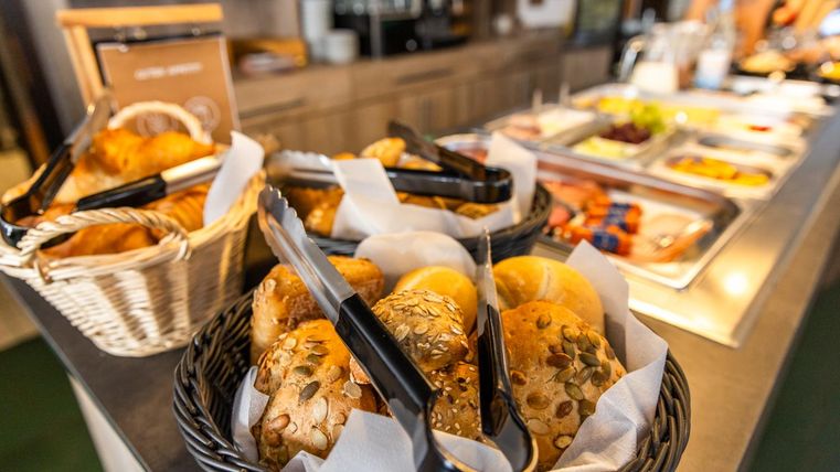 A buffet with fresh rolls in baskets. In the background, there are various dishes and snacks.
