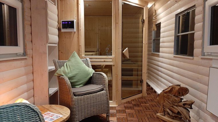 Een gezellige kamer met houten wanden, een comfortabele fauteuil en een sauna. De sfeer is warm en uitnodigend.