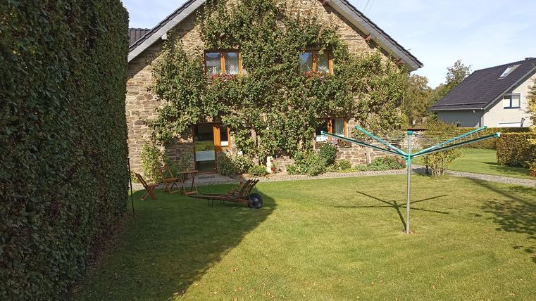 Ein gemütliches Haus mit einer begrünten Fassade und großen Fenstern. Im Garten steht eine Wäschespinne und der Rasen ist gepflegt.
