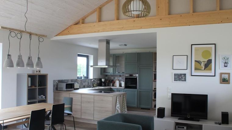 A modern living room with an open kitchen. The decor is bright and stylish, featuring a large dining table and cozy seating.