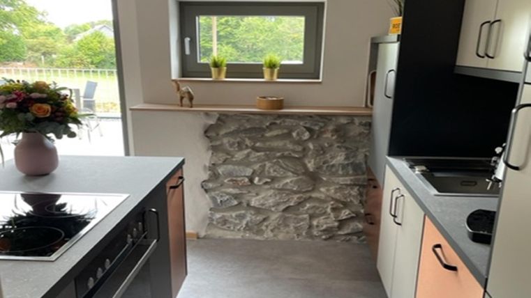 Een moderne keuken met een gemengd ontwerp van hout en steen. Door het raam is een groene uitzicht zichtbaar.