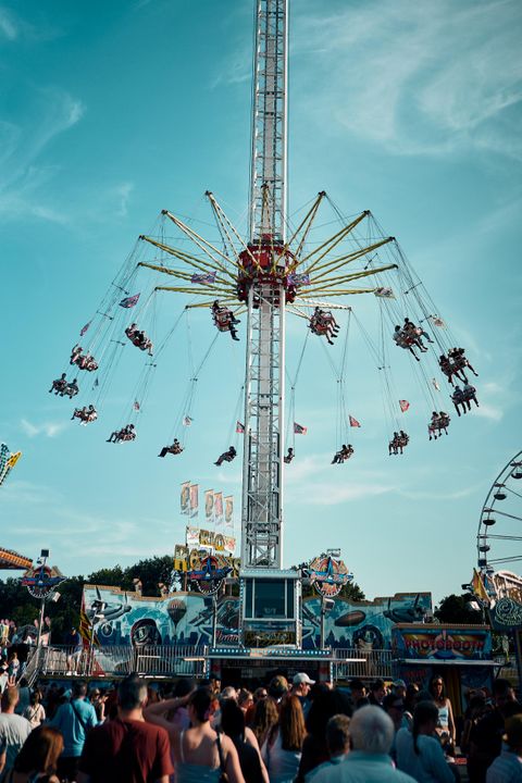 Ein aufregendes Fahrgeschäft auf einem Jahrmarkt, das Schwinger in die Höhe hebt. Viele Menschen stehen in der Nähe und beobachten das Geschehen.