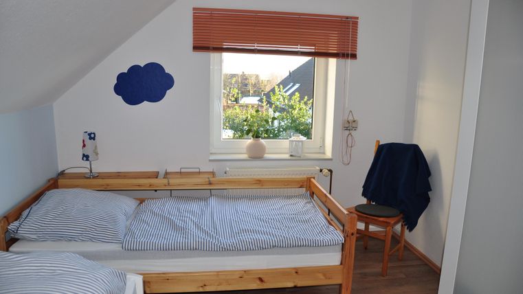 A cozy bedroom with two beds and blue striped bed linens. The window offers a view of a green garden.