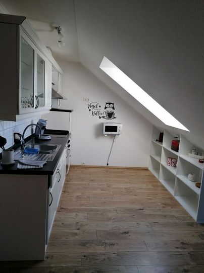 A modern kitchen under the roof with wooden flooring. It includes kitchen furniture, a microwave, and a small dining area.