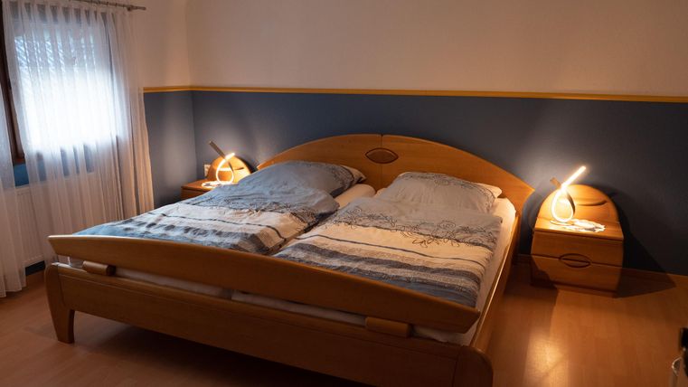 A cozy bedroom with a double bed and nightstands. The walls are painted blue, and soft light shines from the lamps.
