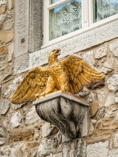 Eine goldene Skulptur eines Greifens sitzt auf einem Mauerwerk. Der Greif hat ausgebreitete Flügel und blickt majestätisch.