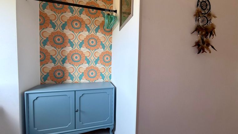 Een stijlvolle hal met een blauwe kast en een kleurrijk, bloemachtig wandtapijtpatroon. Aan de muur hangt een dromenvanger.