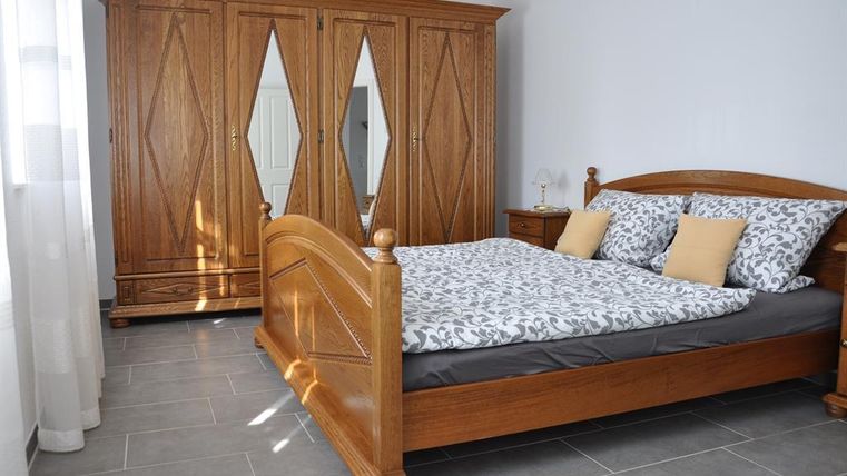 Ein gemütliches Schlafzimmer mit einem großen, hölzernen Bett und einem Kleiderschrank. Die Wände sind hell, und das Licht strahlt durch die Fenster.