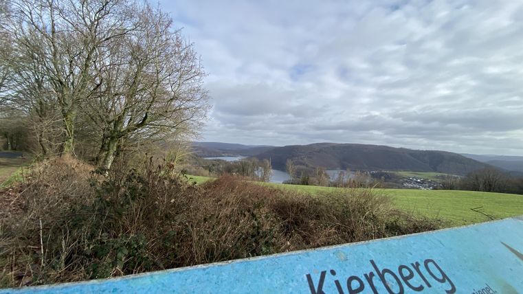 Eine Aussicht auf die Hügel und das Tal von Kierberg. Im Vordergrund ist ein Informationsschild sichtbar, das die Überhöhung anzeigt.