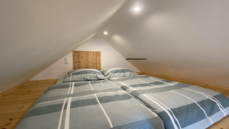 Een gezellige slaapkamer op de zolder met een tweepersoonsbed en lichte wanden. Het beddengoed heeft een modern, gestreept patroon.