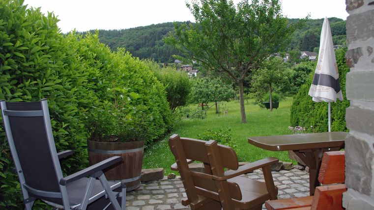 A cozy garden with comfortable chairs and a table. In the background, there are trees and a green meadow.