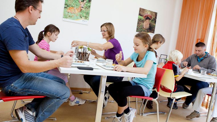A group of children and adults is sitting at a table and painting. There is a creative atmosphere in a bright room.