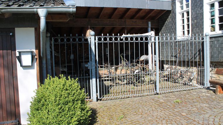 An entrance with a metal gate and a privacy screen. In the background, wooden scraps and a building are visible.