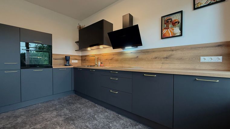 Een moderne keuken met donkere kasten en een houten werkblad. Aan de muur hangen twee schilderijen, en er is een wandkast boven de kookplaat.