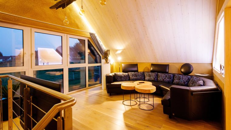 A cozy living space with a large, dark sofa and two small tables. Large windows offer a view of the surroundings and provide plenty of natural brightness.