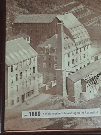 Een historische foto van fabrieksgebouwen in Rosenthal voor 1880. De locatie toont meerdere gebouwen en een hoge schoorsteen.