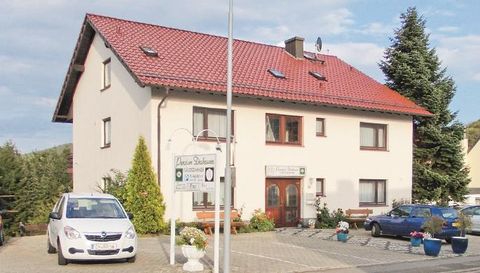 Een twee-onder-een-kapwoning met een rood dak en meerdere ramen. Voor het huis staan voertuigen en bloeiende planten in potten.