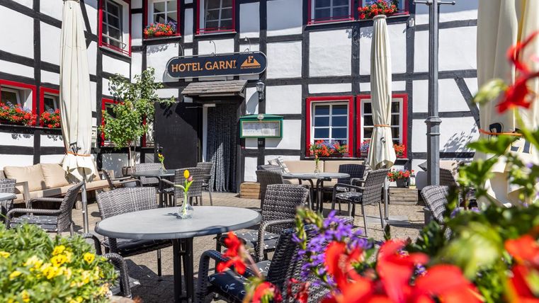 A cozy terrace in front of a hotel with beautiful plants and flowers. There are tables and chairs that invite you to relax.