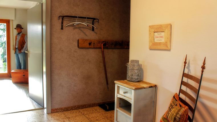 Een uitnodigende hal met een open deur en een meubelstuk. Aan de muur hangen een kapstok en een decoratief bord.