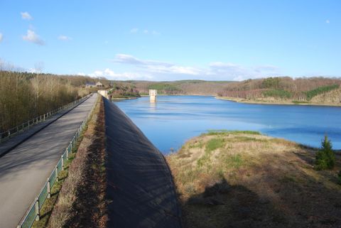Een rustige reservoir omgeven door bossen en heuvels. Een geasfalteerde weg loopt langs de oever.