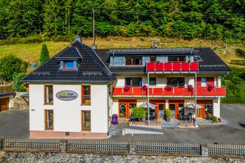 Een charmant hotel met rode balkons in een groene omgeving. De gevel ziet er uitnodigend en vriendelijk uit.